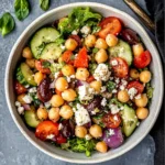 Freshly prepared Chickpea Greek Salad with colorful vegetables, creamy feta, and a zesty dressing, served in a white bowl.