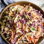 Classic coleslaw served in a white bowl with a mix of green and purple cabbage, carrots, and creamy dressing.