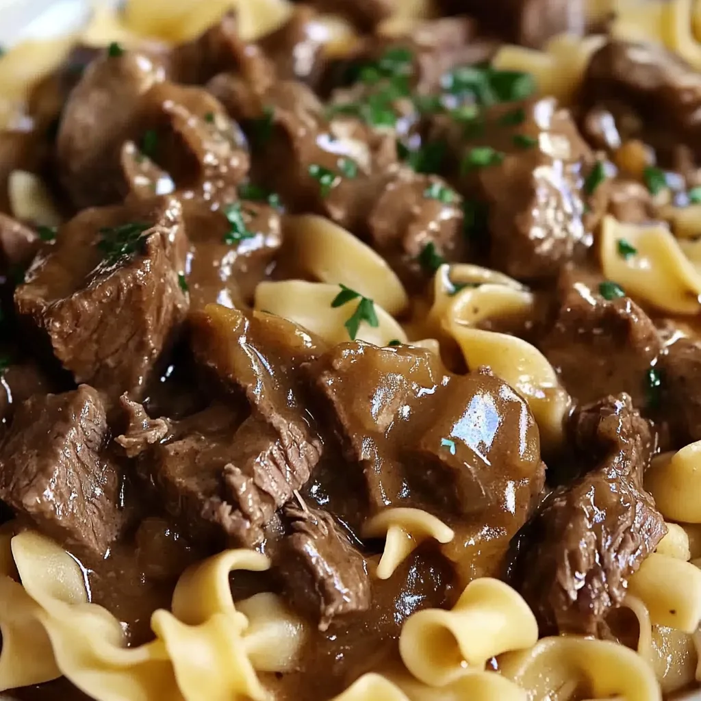 Tender Crockpot Beef Tips served over buttery egg noodles with fresh parsley garnish.