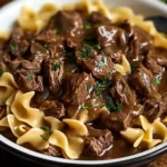 Tender Crockpot Beef Tips served over buttery egg noodles with fresh parsley garnish.