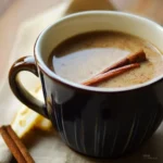 A cozy mug of cinnamon sore throat tea garnished with a cinnamon stick and a slice of lemon, steaming on a wooden table.