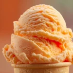 Bowl of creamy Orange Crush Sherbet with a scoop topped by orange slices and fizzy soda bubbles
