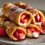 Strawberry French Toast Roll-Ups on a white plate topped with fresh berries and maple syrup