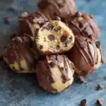 No-bake chocolate chip cookie dough truffles on a white plate, coated in dark chocolate and sprinkled with mini chocolate chips.