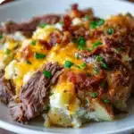 Cheesy Crockpot Loaded Steak and Potato Bake topped with crispy bacon and green onions.