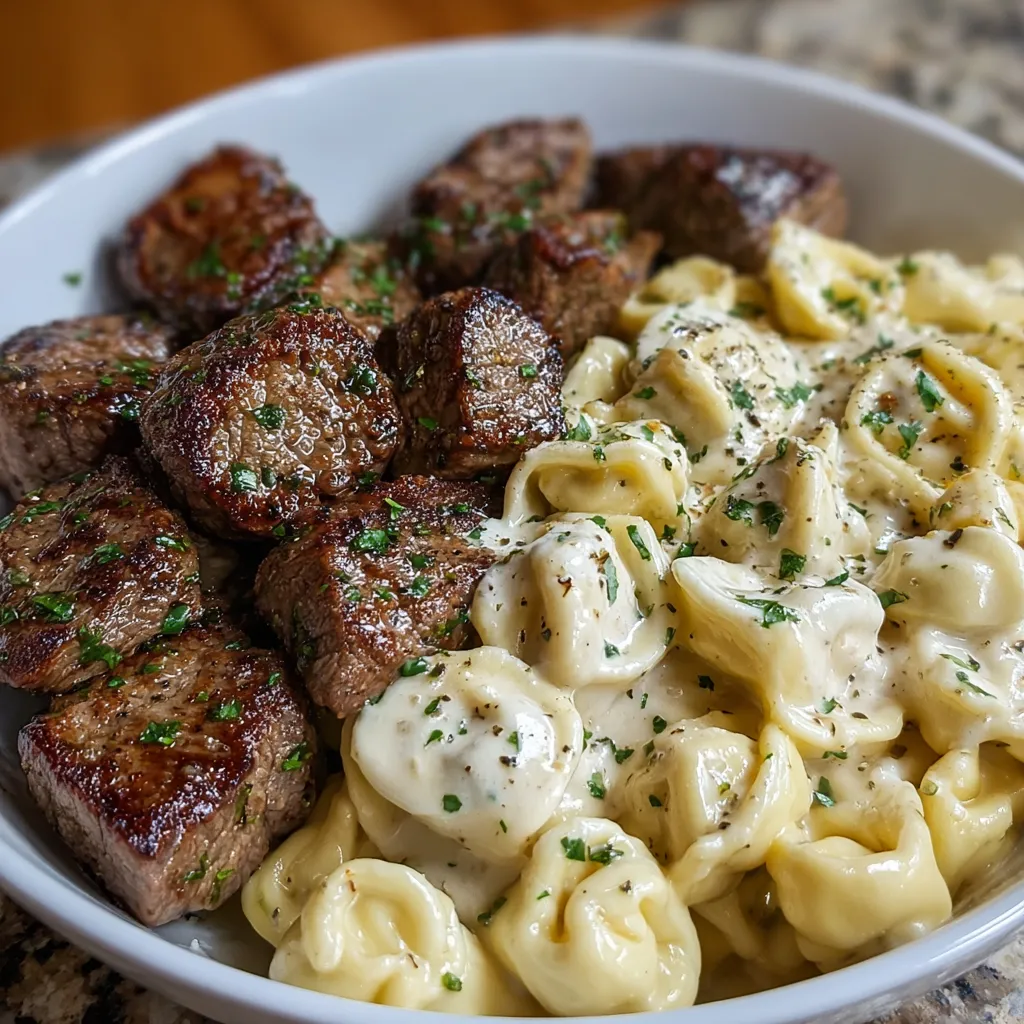 Creamy garlic butter steak bites served with tortellini in Alfredo sauce in a white skillet.