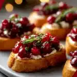 Crispy holiday cranberry crostini topped with creamy cheese, cranberry sauce, honey drizzle, and fresh rosemary.