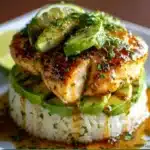 Honey lime chicken and avocado rice stack served on a plate, topped with lime wedges and fresh cilantro.