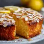 Moist lemon almond cake with glossy lemon glaze, garnished with zest and served on a ceramic plate.