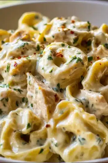 A creamy bowl of Crockpot Chicken Alfredo Tortellini garnished with fresh parsley and Parmesan.