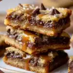 Gooey Chocolate Chip Caramel Butter Bars stacked on a white plate with a drizzle of melted caramel.