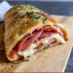 Golden baked homemade stromboli filled with mozzarella and Italian meats on a wooden board