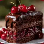 Slice of Ultimate Chocolate Cherry Cake with dark chocolate ganache dripping and fresh cherries on top