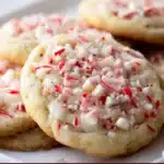 White Chocolate Peppermint Cookies — soft, golden cookies with white chocolate chips and red crushed candy cane pieces on a parchment-lined baking sheet